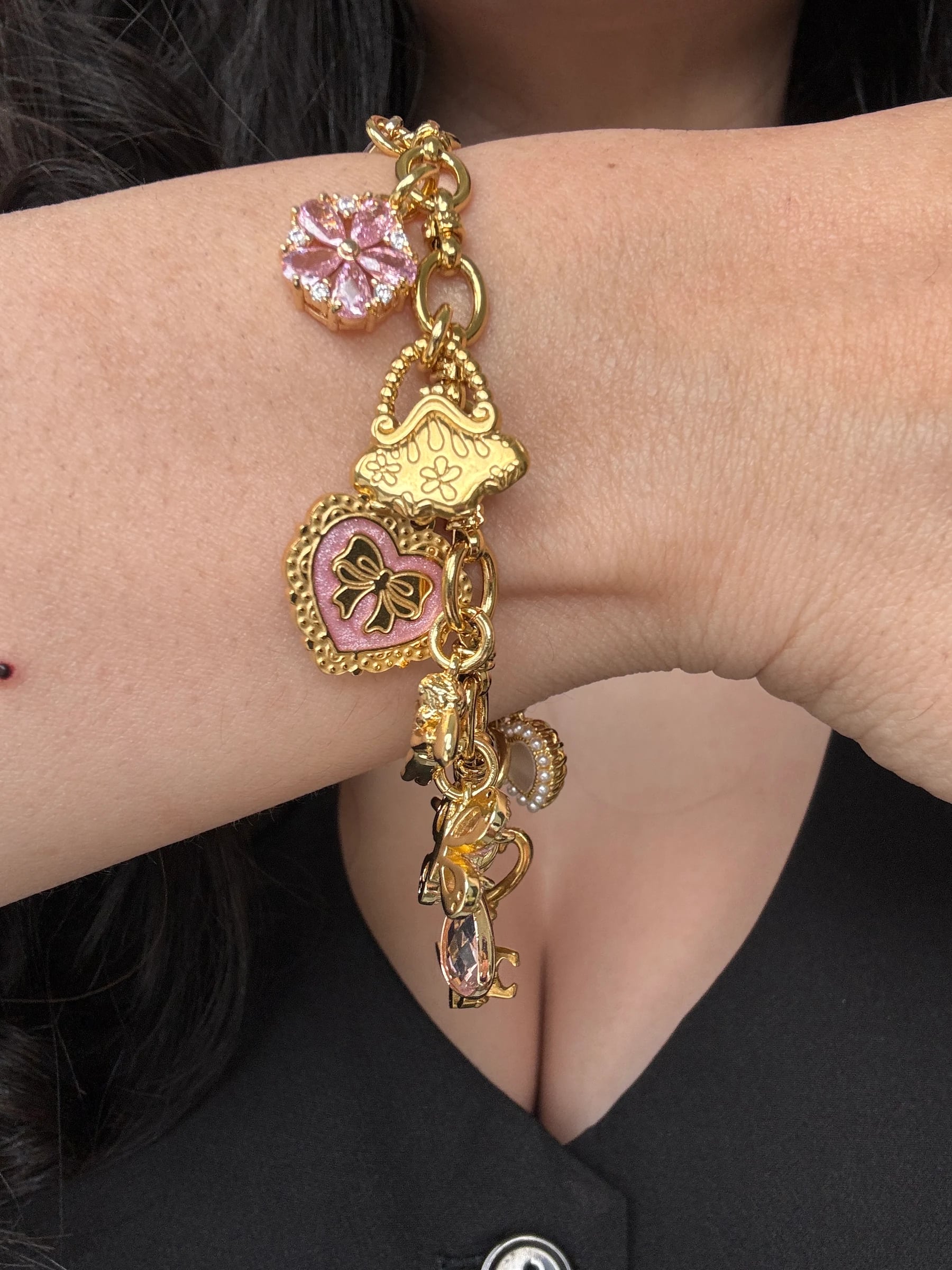 Woman's wrist with an 18k gold plated charm bracelet featuring pink crystal flower and heart charms, by Enleira