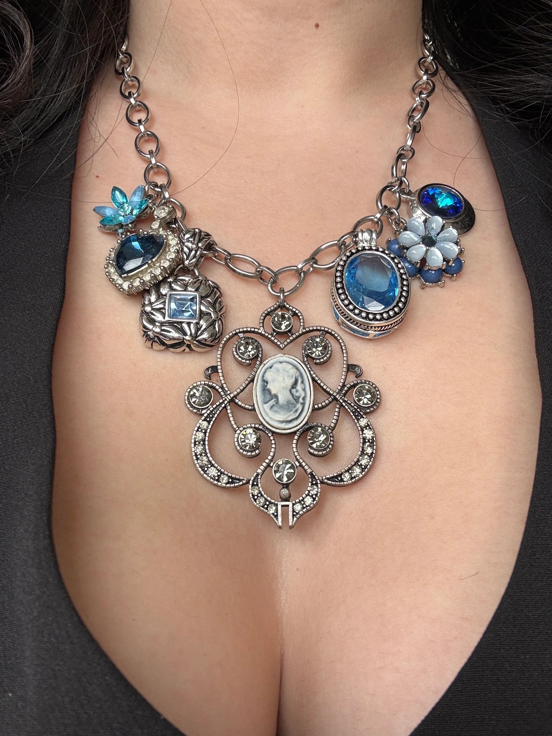 Stainless steel charm necklace with a vintage cameo and blue crystal charms, worn on a woman's neckline, by Enleira.
