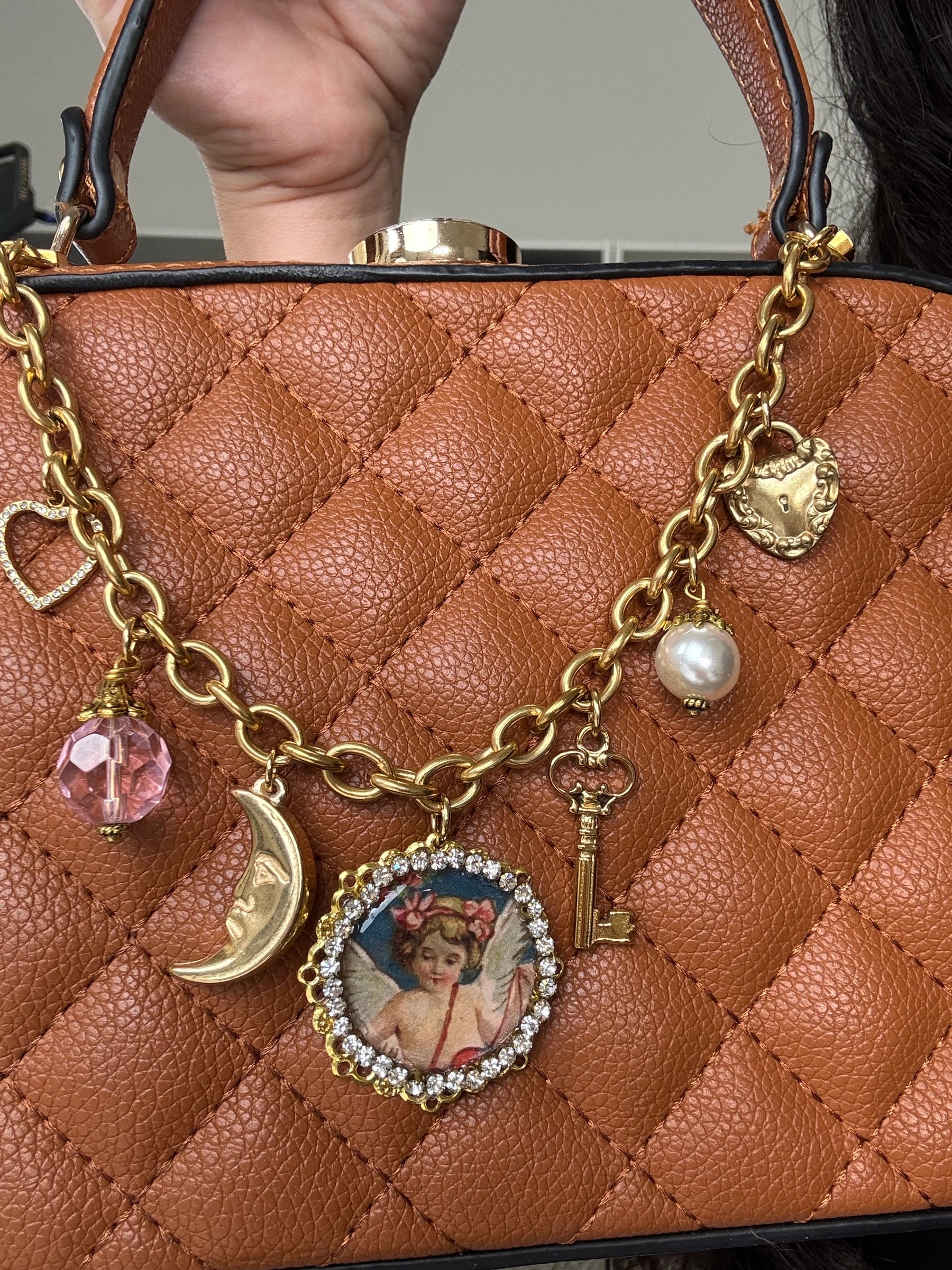 18k gold plated purse chain with angel, heart, and key charms on a quilted brown handbag, by Enleira