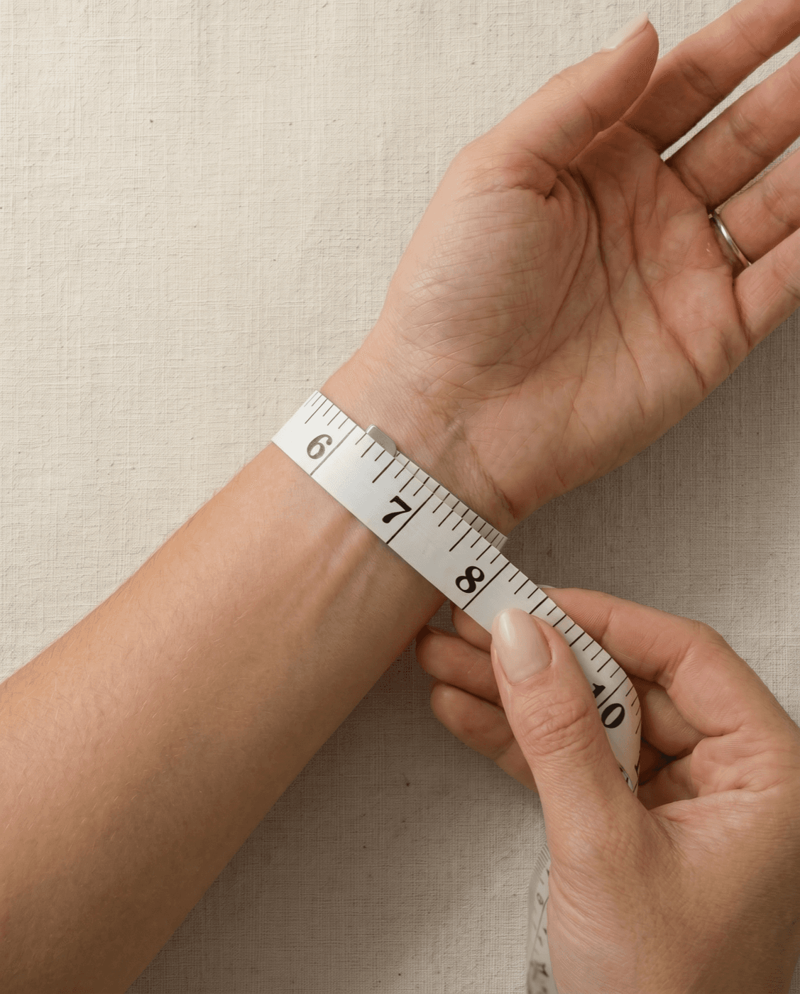 Two hands wrapping a soft white tape measure snugly around a wrist to measure wrist circumference for a bracelet fit
