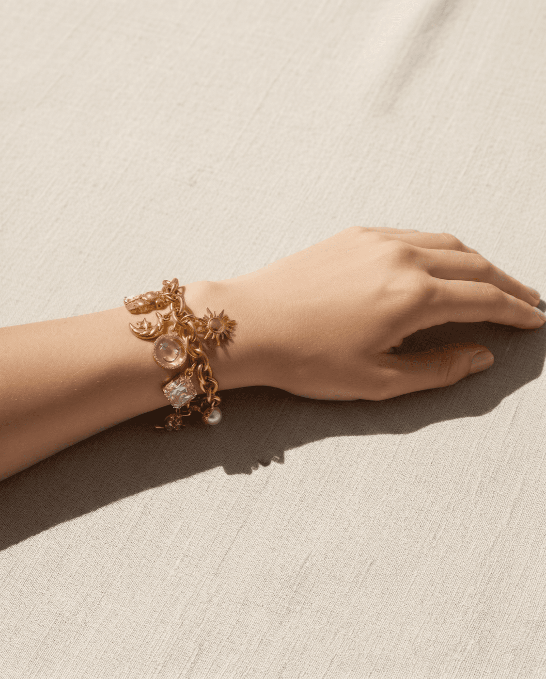 A delicate gold-toned charm bracelet on a wrist beside a cream tape measure on linen