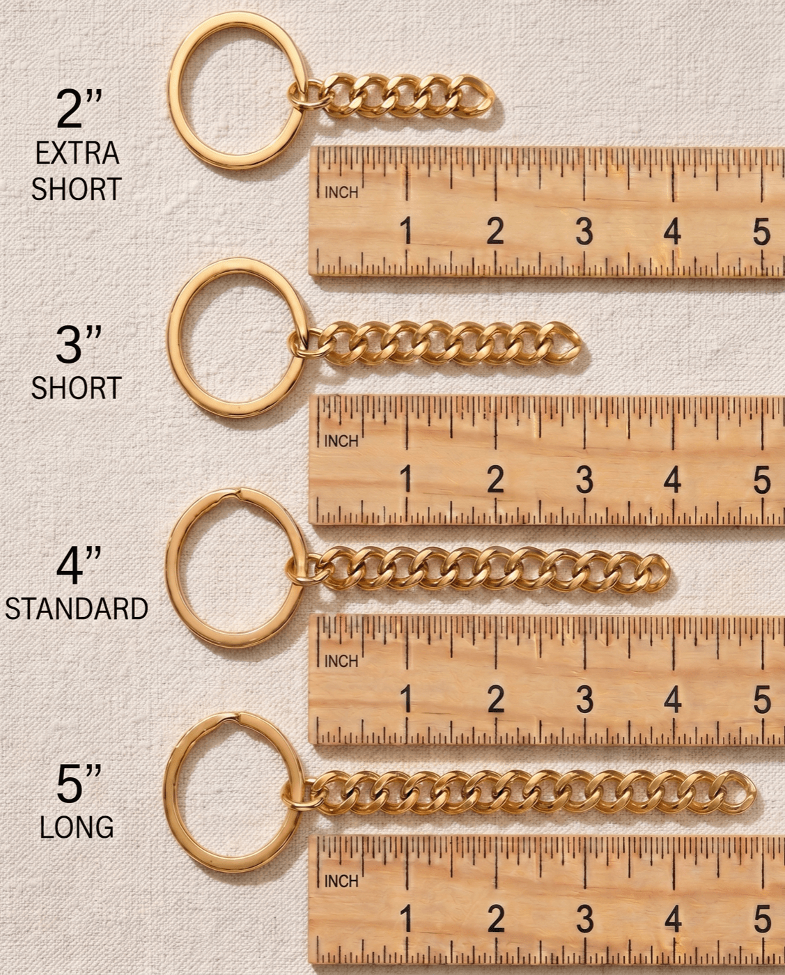 Four gold curb-chain keychain loops shown in size order against a wooden ruler on cream linen