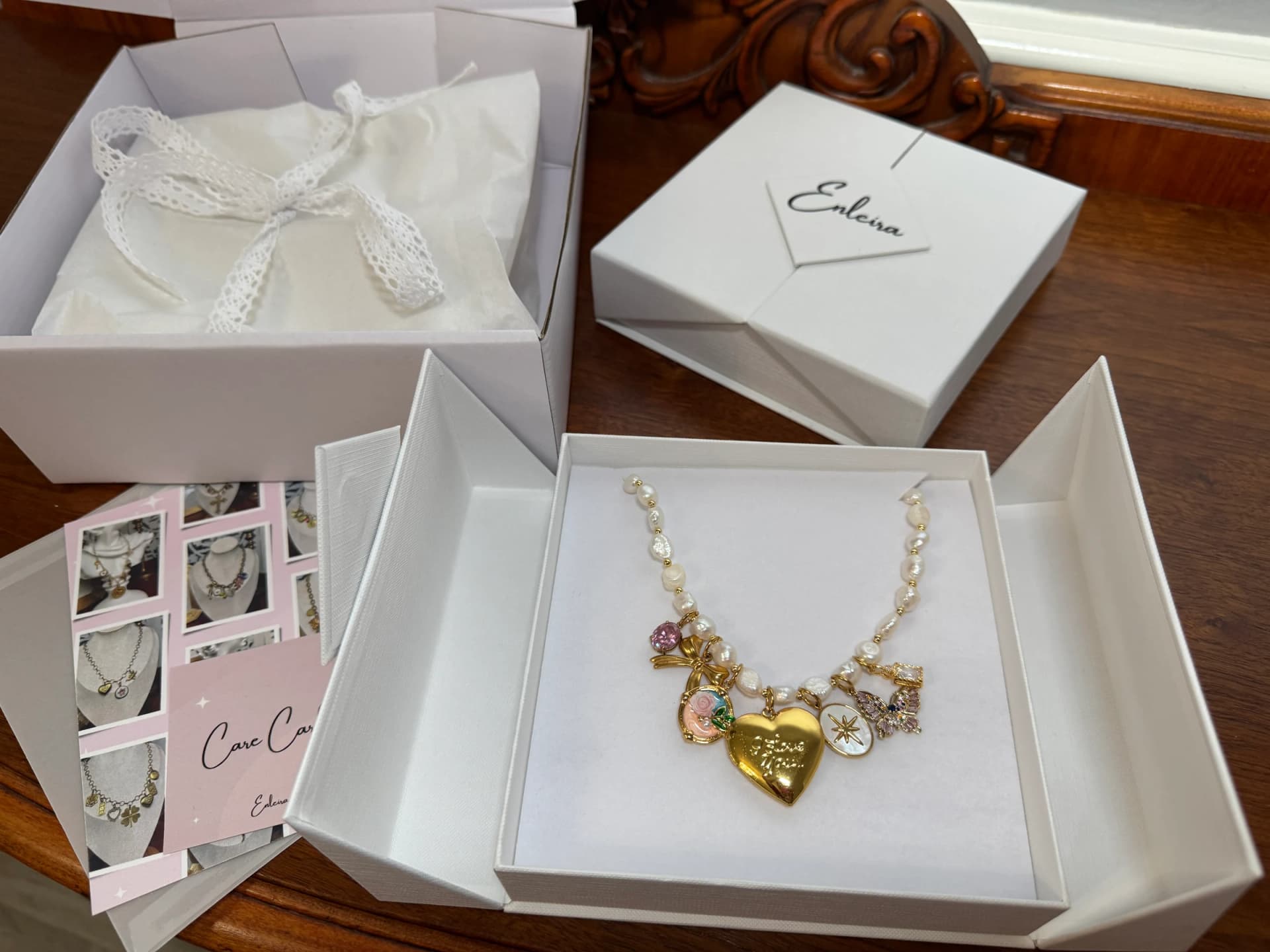 A handcrafted pearl charm necklace with a gold heart locket displayed in a white gift box, by Enleira