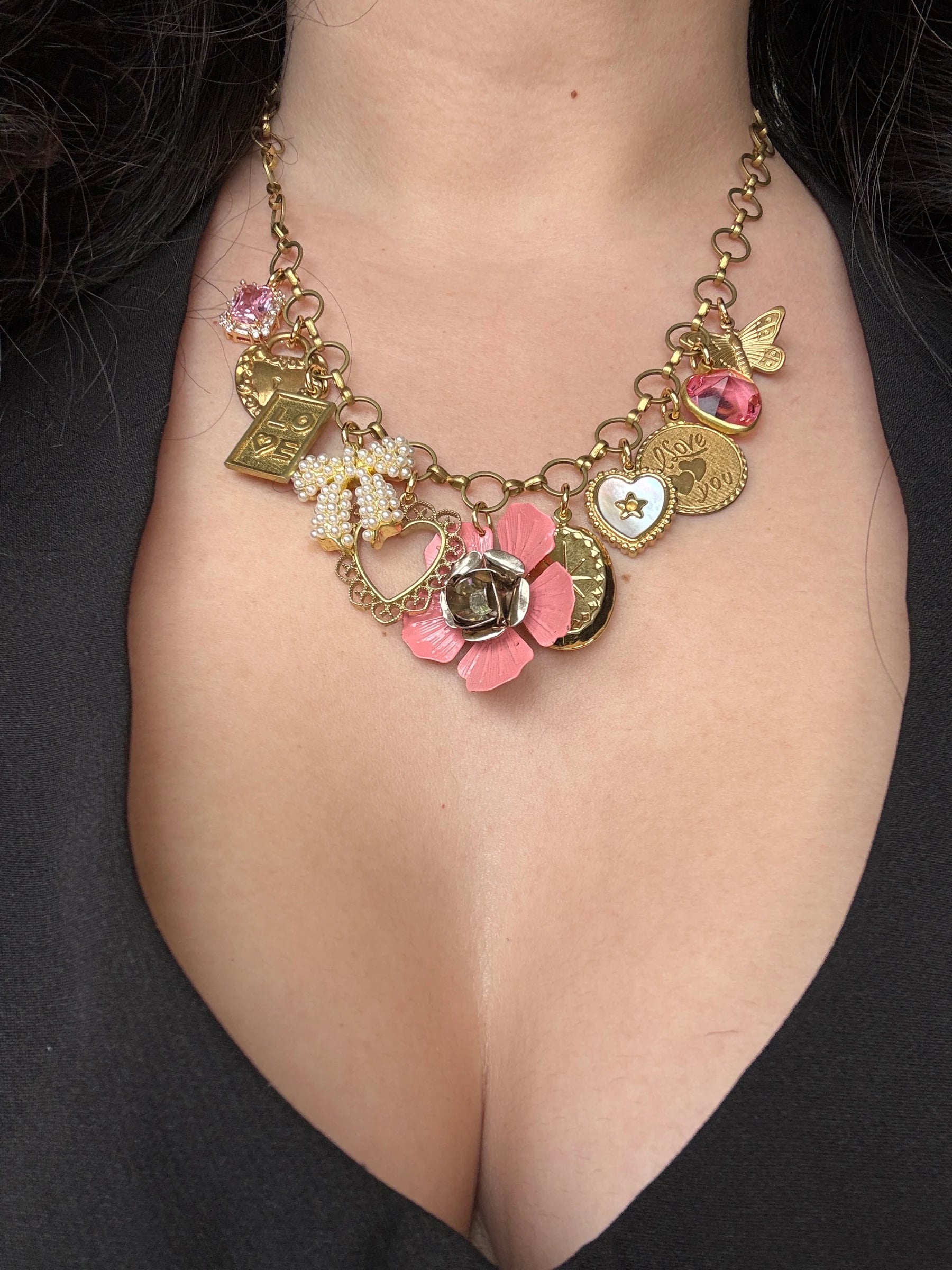 Woman wearing a custom 18k gold plated charm necklace with pink flower and heart charms, by Enleira