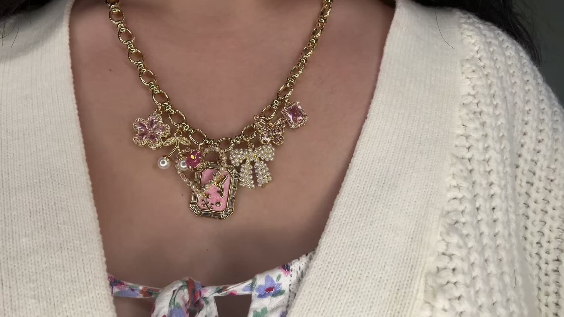 Woman wearing a custom 18k gold plated charm necklace with pink flower, bow, and butterfly charms, by Enleira